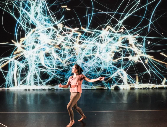 A photo of Jan-Ming Lee dancing on stage at The Place with computer rendered visuals projected behind, taken during a performance of This Floating World by Tim Murray-Browne and Jan-Ming Lee. Photo by Tadeo Sendon.