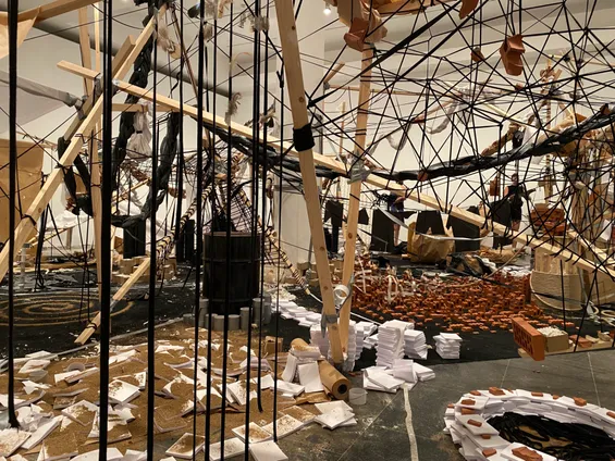 Photo of the first installation at Cinthia Marcelle's exhibition 'A Conjunction of Factors'. It shows a messy array of wood, rope, bricks, tiles, dirt and gaffa tape strung up around the room. Photo by Tim Murray-Browne.