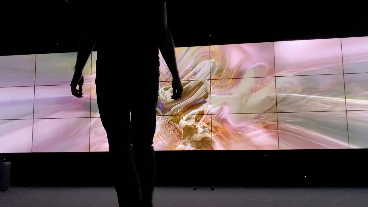 A photo of SELF ABSORBED, an interactive installation by Tim Murray-Browne. A man stands in front of a video wall showing an abstract image rendered in real-time in response to the man's movements.