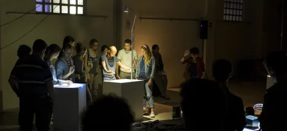 The interactive sound installation “Cave of Sounds” Tim Murray-Browne and the Music Hackspace Ensemble. A man stands in front of a plinth casting shadows on it with his hands, at the edge of an art installation. People stand around watching him. Photo: Tim Murray-Browne