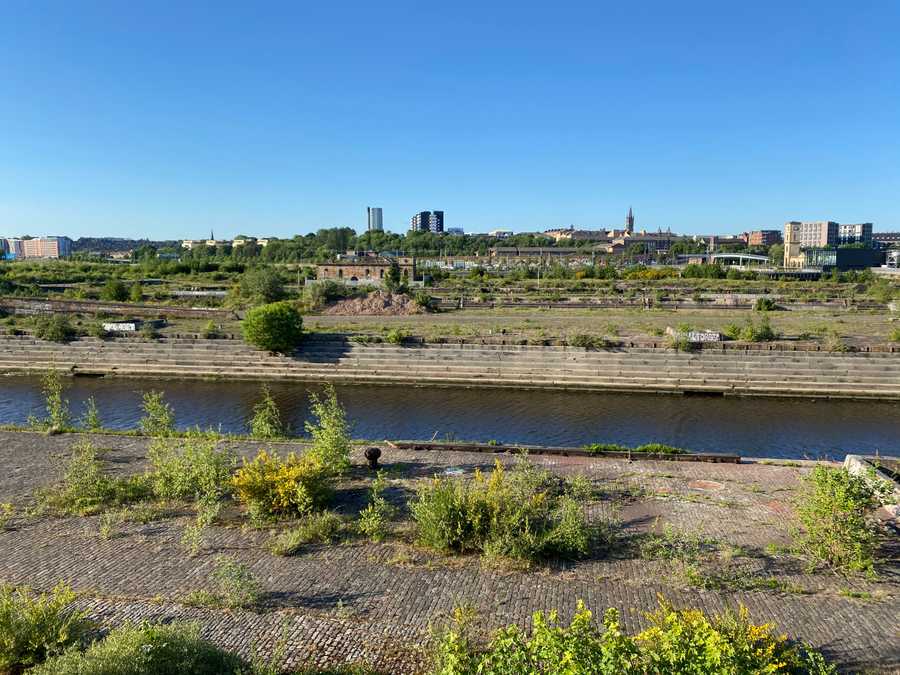 A photo of the derelict shipyard at Glasgow with green plants growing through the gaps in the brickwork floor. Photo (c) 2022 Tim Murray-Browne.