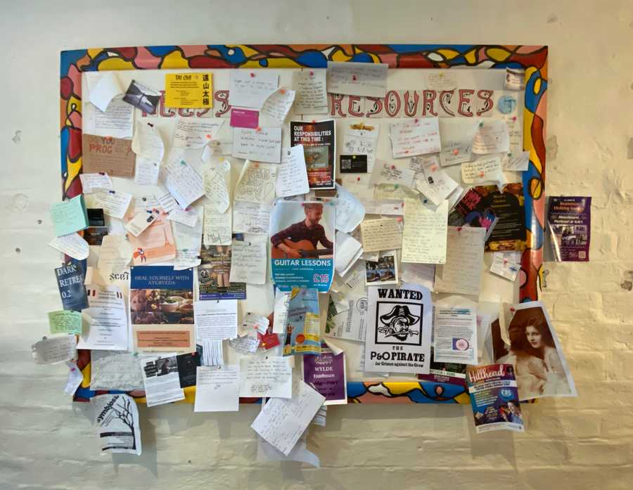 A photo of a noticeboard on a wall crowded with different pieces of paper in different styles. Photo (c) 2022 Tim Murray-Browne.